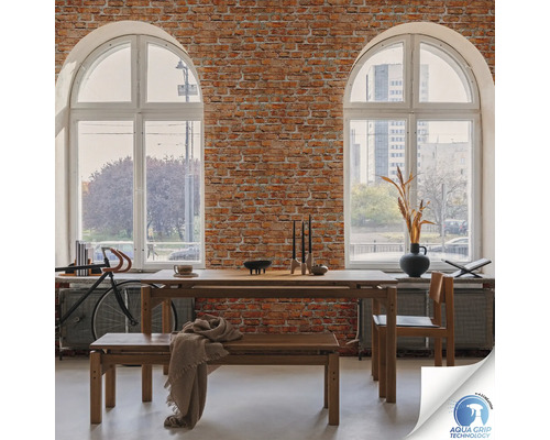Salle à manger avec table en bois, banc et chaise devant un mur de briques avec deux grandes fenêtres