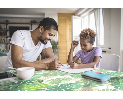 Père aidant son enfant à faire ses devoirs à une table avec un motif de feuilles