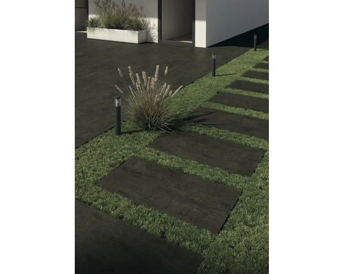 Des dalles de terrasse en pierre forment un chemin dans un jardin, éclairé par des lampes de jardin.