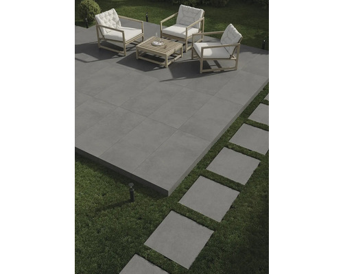 Terrasse avec carrelage gris, salon de jardin avec cadre en bois et coussins blancs, et pas japonais dans la pelouse.