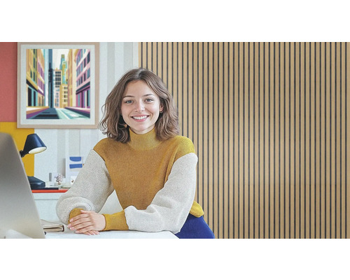 Une femme sourit à un bureau devant un mur de panneaux de bois.