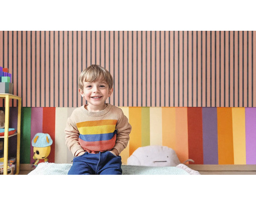 Un enfant se tient devant un mur à rayures verticales dans une chambre d''enfant.