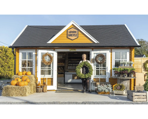 Une cabane de jardin jaune avec une femme tenant une couronne et des citrouilles devant.