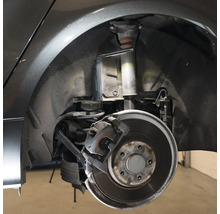 Detailaufnahme eines Autos mit freigelegtem Radkasten, Stoßdämpfer und Bremse, beleuchtet mit einer Arbeitsleuchte.