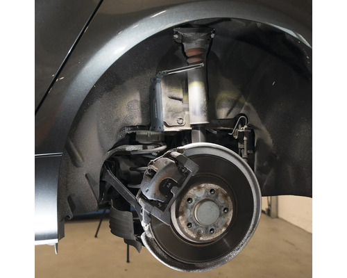 Detailaufnahme eines Autos mit freigelegtem Radkasten, Stoßdämpfer und Bremse, beleuchtet mit einer Arbeitsleuchte.