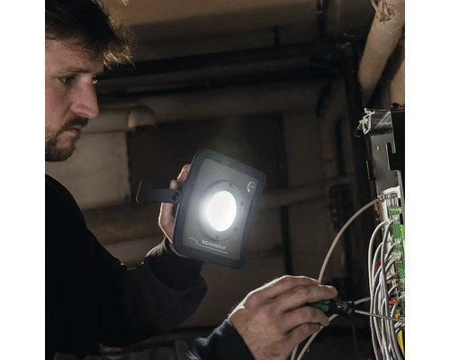 Ein Mann repariert eine elektrische Anlage mit einem Schraubendreher und einer Scangrip Arbeitsleuchte
