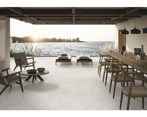 Grande terrasse avec sol carrelé, chaises longues, table et chaises avec vue sur la mer.