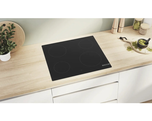 Plaque de cuisson noire avec quatre zones de cuisson dans une cuisine claire.