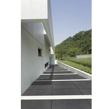 Aussenbereich mit grauen Bodenplatten, einem weißen Gebäude und einer grünen Hügellandschaft