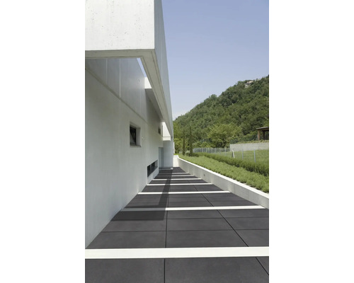 Aussenbereich mit grauen Bodenplatten, einem weißen Gebäude und einer grünen Hügellandschaft