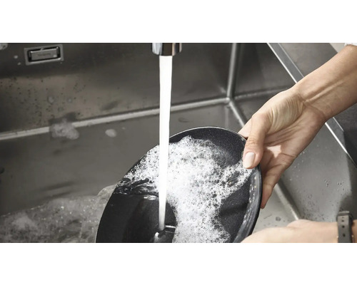Une personne lave une poêle à frire dans un évier sous l''eau courante.