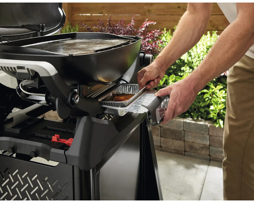 Mann schiebt eine Aluschale in einen Gasgrill.