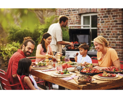Famille appréciant un repas en plein air avec un barbecue en arrière-plan