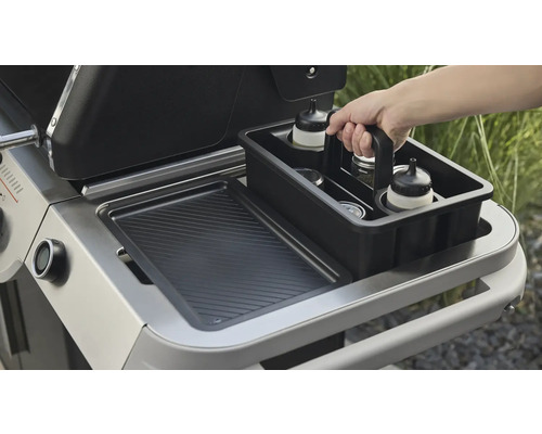 Une personne range des accessoires de barbecue dans un récipient noir à côté d''un barbecue.