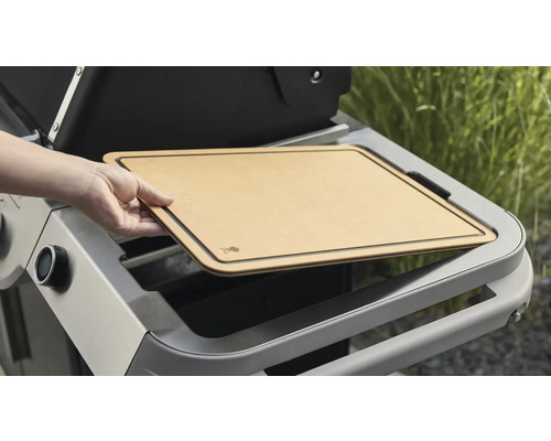 Une personne place une planche à découper sur un chariot de barbecue.
