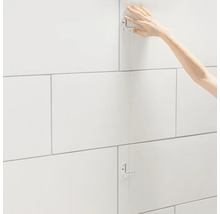 Fliesenleger beim Verlegen von Wandfliesen mit Fliesenlehre