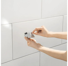 Hände installieren einen Magnet-Türfeststeller an einer gefliessten Wand.