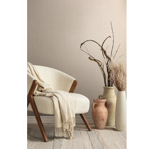 Intérieur décoratif avec fauteuil, plaid, vases et graminées ornementales devant un mur avec papier peint textile.