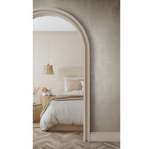 Helle Schlafzimmerszene mit Bett, Nachttisch und geflochtener Pendelleuchte, gesehen durch einen Torbogen