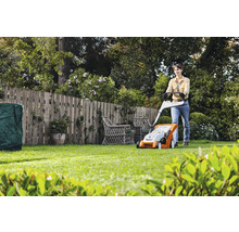 Une femme utilise une tondeuse à gazon dans un jardin avec une clôture en bois.