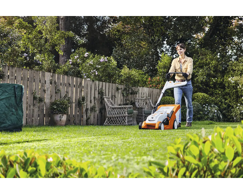 Eine Frau benutzt einen Rasenmäher im Garten mit Holzzaun.