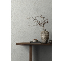 Detailansicht einer dekorierten Wand mit floral gemusterter Tapete, einem Holztisch mit Dekorationsgegenständen und einer Vase mit Zweigen.