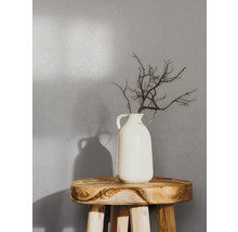 Dekorative Zweige in einer weißen Vase auf einem Holzhocker