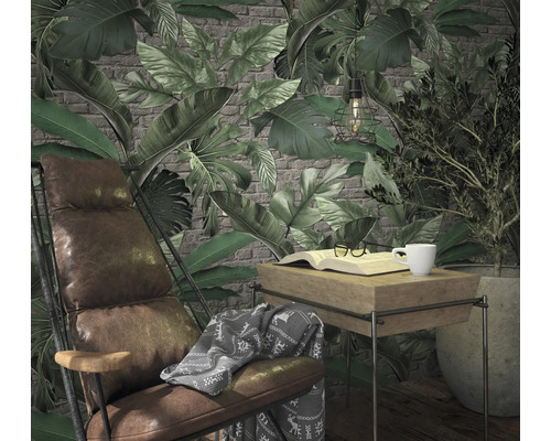 Scène de salon avec fauteuil, table, livre, tasse et plantes devant un papier peint à motifs de feuilles