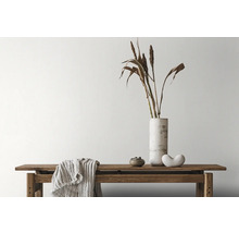 Dekorative Anordnung mit Bank, Vase, Ziergras und Textilien im Innenraum.