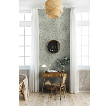 Dekoratives Interieur mit einem Holztisch, einem runden Spiegel und einer Tapete mit Blättermuster in einem hellen Raum