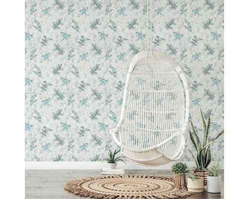 Pièce décorative avec papier peint floral, fauteuil en rotin et tapis rond.