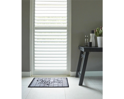 Scène avec des jalousies de porte, un paillasson avec l''inscription Bienvenue et une table d''appoint avec des articles de décoration