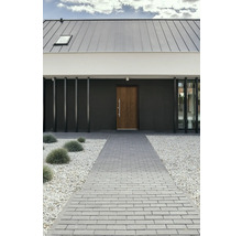 Fassadenansicht eines modernen Hauses mit grauer Steinfassade, Holztür, Steindach und gepflastertem Gehweg.