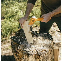 Eine Person spaltet Holz mit einer Spaltaxt auf einem Hackklotz.