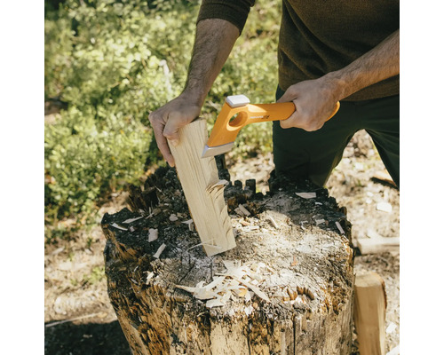 Eine Person spaltet Holz mit einer Spaltaxt auf einem Hackklotz.