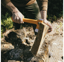 Eine Person spaltet mit einer Spaltaxt Holz auf einem Hackklotz.