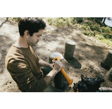 Mann sitzt im Wald und hält eine Axt.