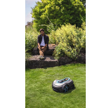Scène avec un robot tondeuse sur une pelouse et une personne assise sur des rochers
