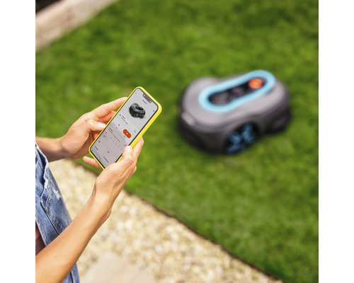Person steuert einen Gardena Mähroboter mit einem Smartphone im Garten.