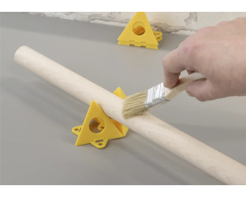 Rundholz fixiert in Dreieckstützen wird mit Pinsel bearbeitet