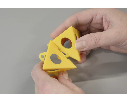 Zwei gelbe Fliesenausrichtungshilfen werden von zwei Händen gehalten.