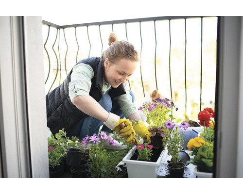 Une femme plante des fleurs sur un balcon avec diverses fleurs et jardinières.