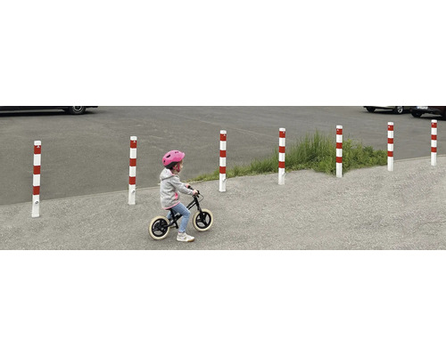 Plusieurs bornes d''arrêt rayées rouge et blanc délimitent une zone, tandis qu''un enfant passe devant avec une draisienne.
