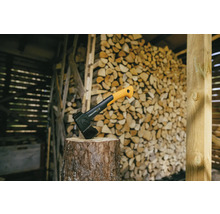 Merlin à fendre sur une bûche devant une pile de bois