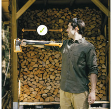 Un homme tient une hache à fendre Fiskars X25 dans sa main tendue devant une pile de bois. L''accent est mis sur la bonne longueur de bras.