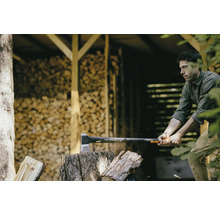 Un homme fend du bois avec une hache Fiskars devant une pile de bois
