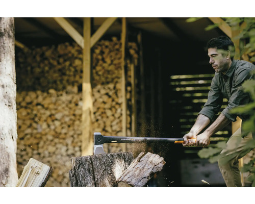 Un homme fend du bois avec une hache Fiskars devant une pile de bois