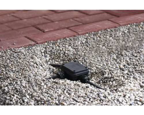 Boîte de dérivation dans un lit de gravier avec un pavé rouge en arrière-plan