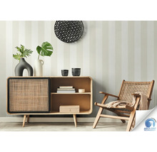 Scène de salon avec commode, décoration et fauteuil en rotin devant un mur rayé