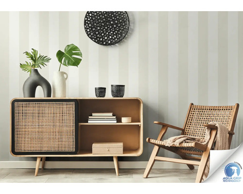 Scène de salon avec commode, décoration et fauteuil en rotin devant un mur rayé